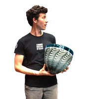 Jared F. Rosenacker, glass artist, holding a large incalmo bowl that is transparent blue on top with a gray and white pattern on the bottom.