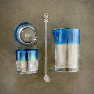 The Mariner Cocktail Set - Alined in a grid, composed of one cocktail mixing glass, one spoon, and two rocks glasses with an ocean blue band of color. 