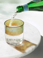 Antique Silver rocks glass with blue / teal color stripe, sitting on top a marble table with seltzer water being poured into it.